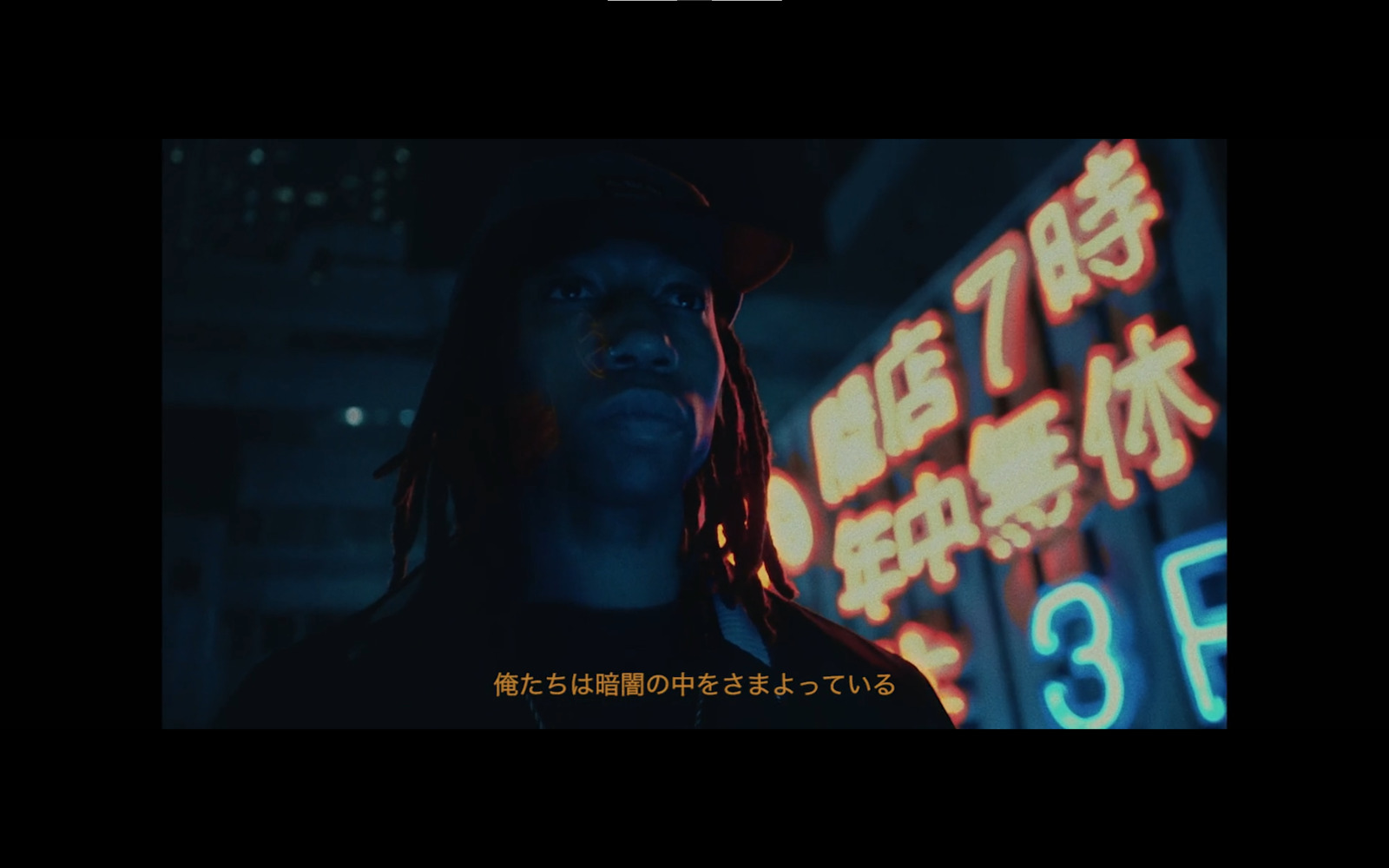 a man with dreadlocks standing in front of a neon sign