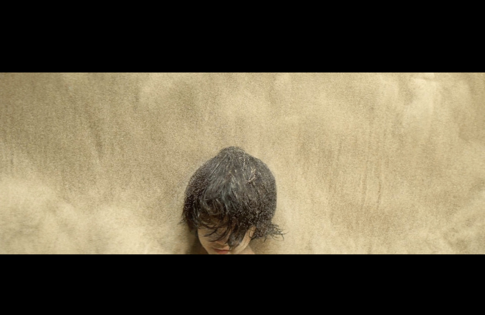 a young boy laying on top of a sandy beach