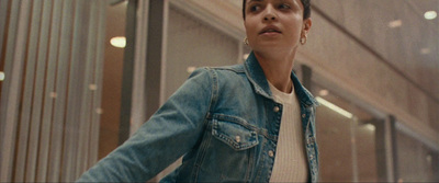 a woman in a denim jacket is walking down a hallway