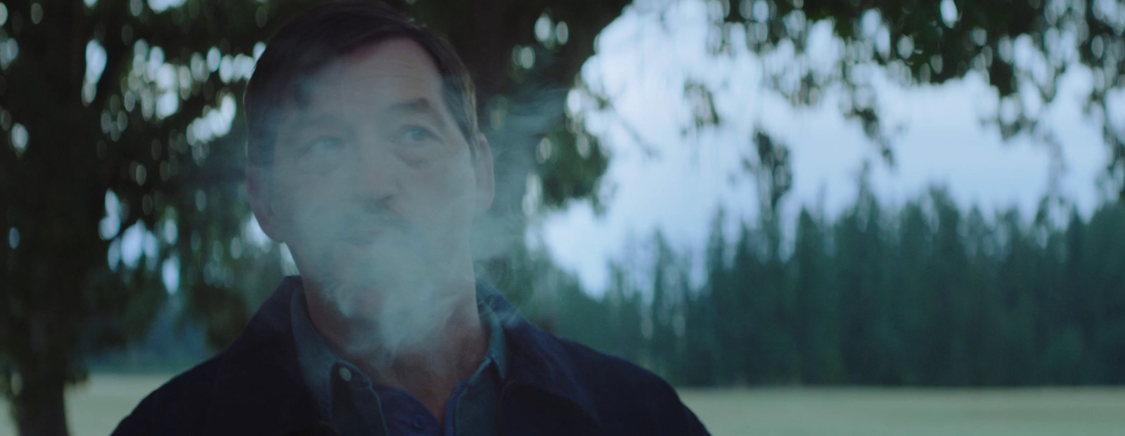 a man standing in front of a tree with smoke coming out of his mouth