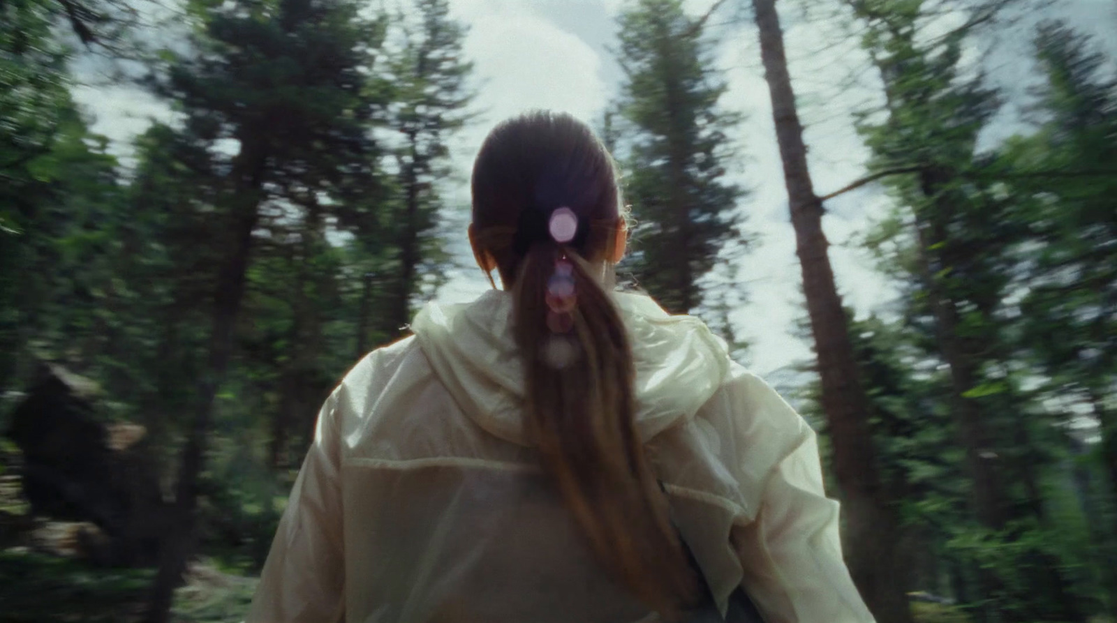 a woman with long hair walking through a forest