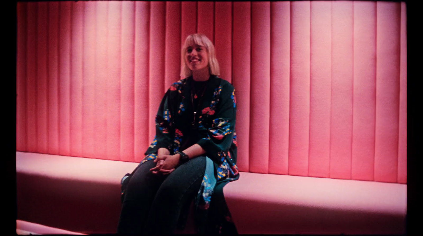 a woman sitting on a bench in front of a red wall