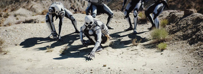 a group of alien like creatures walking across a desert