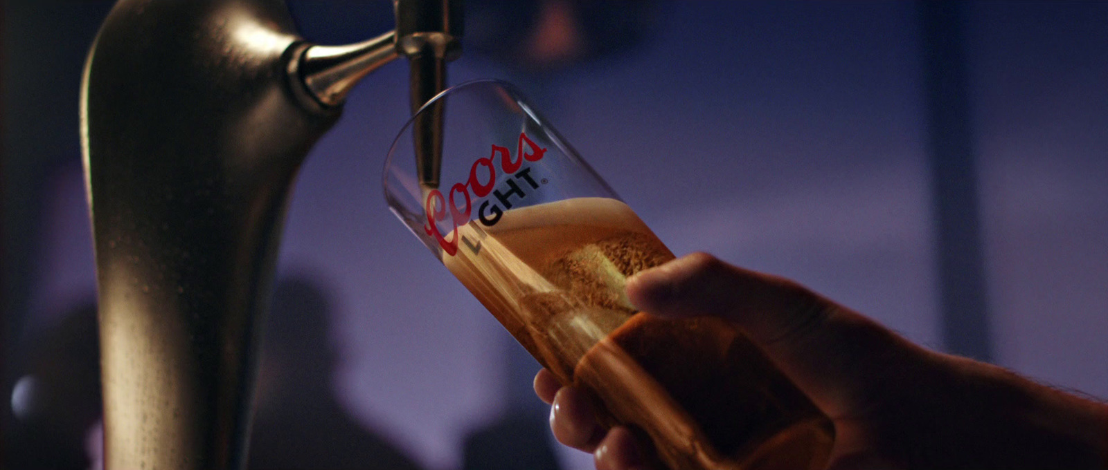 a person holding a glass of beer in front of a faucet