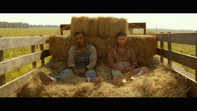 a couple of men sitting on top of a pile of hay