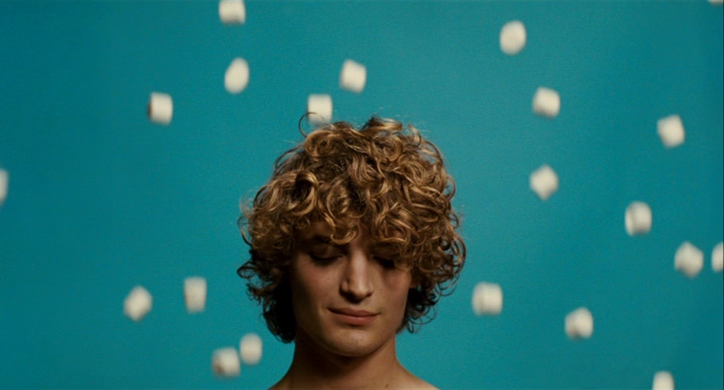 a man with curly hair standing in front of a blue background