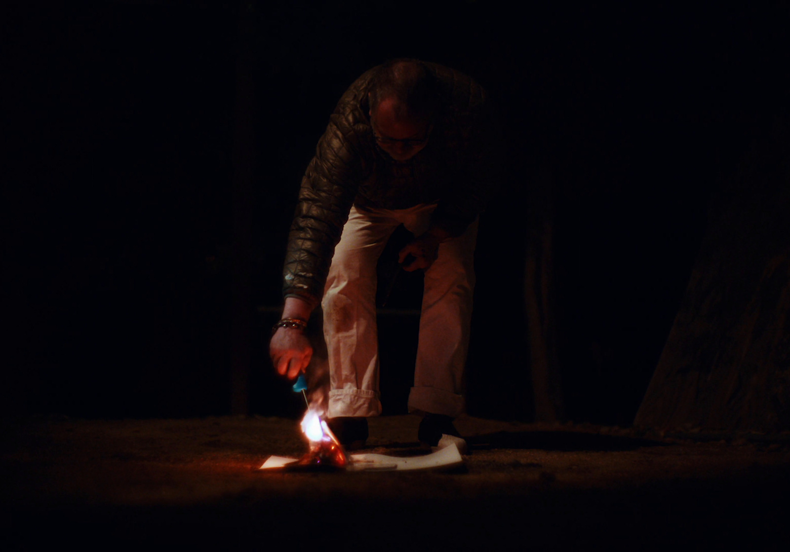 a man standing over a fire in the dark