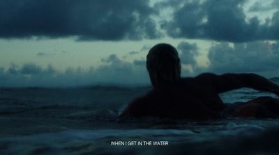 a man sitting in the ocean with a cloudy sky in the background