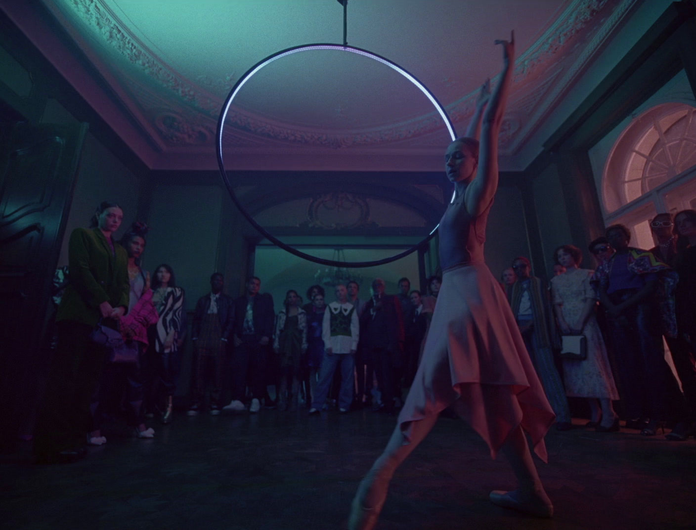 a woman in a long dress holds a hoop above her head as people look on