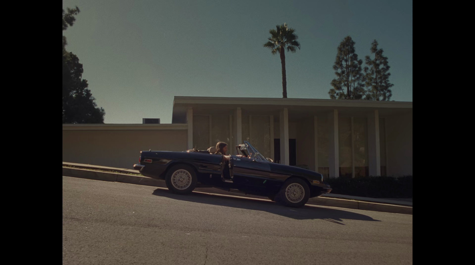 a man driving a convertible car down a street