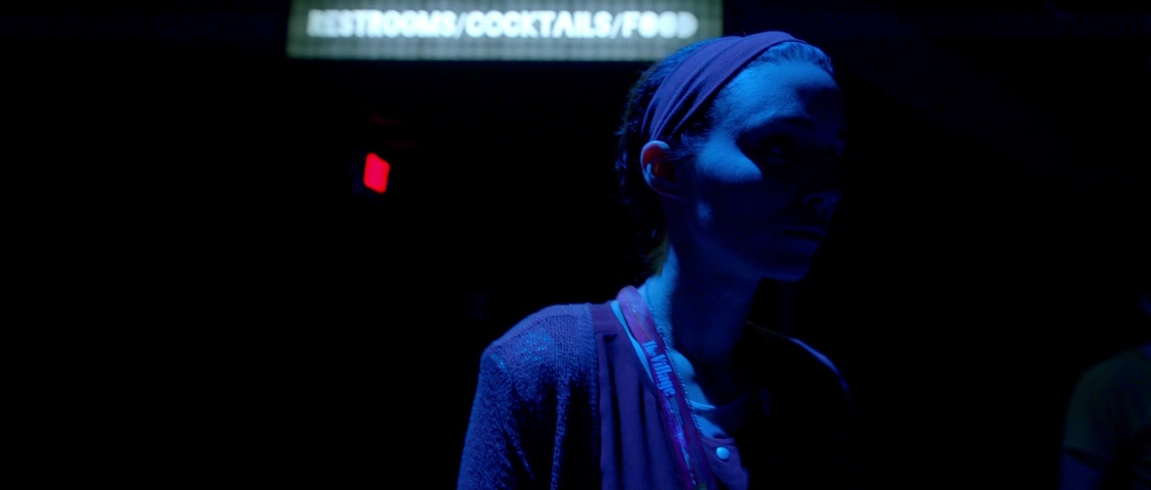 a woman standing in a dark room with a neon sign in the background