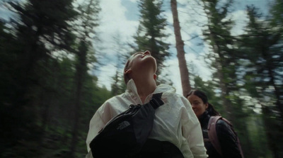 two people walking through a forest with trees in the background