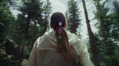 a woman with long hair walking through a forest