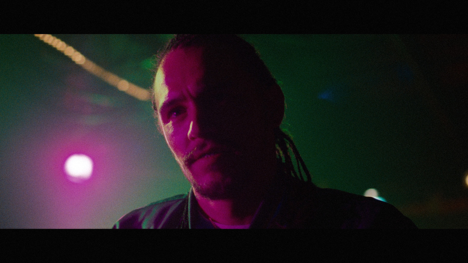 a man with dreadlocks standing in front of a purple and green light