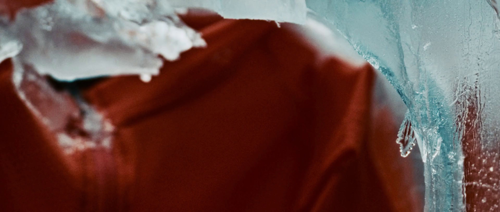 a man in a red jacket standing in front of a wall covered in ice