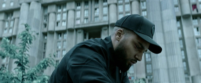 a man in a black jacket and cap looking down at his cell phone