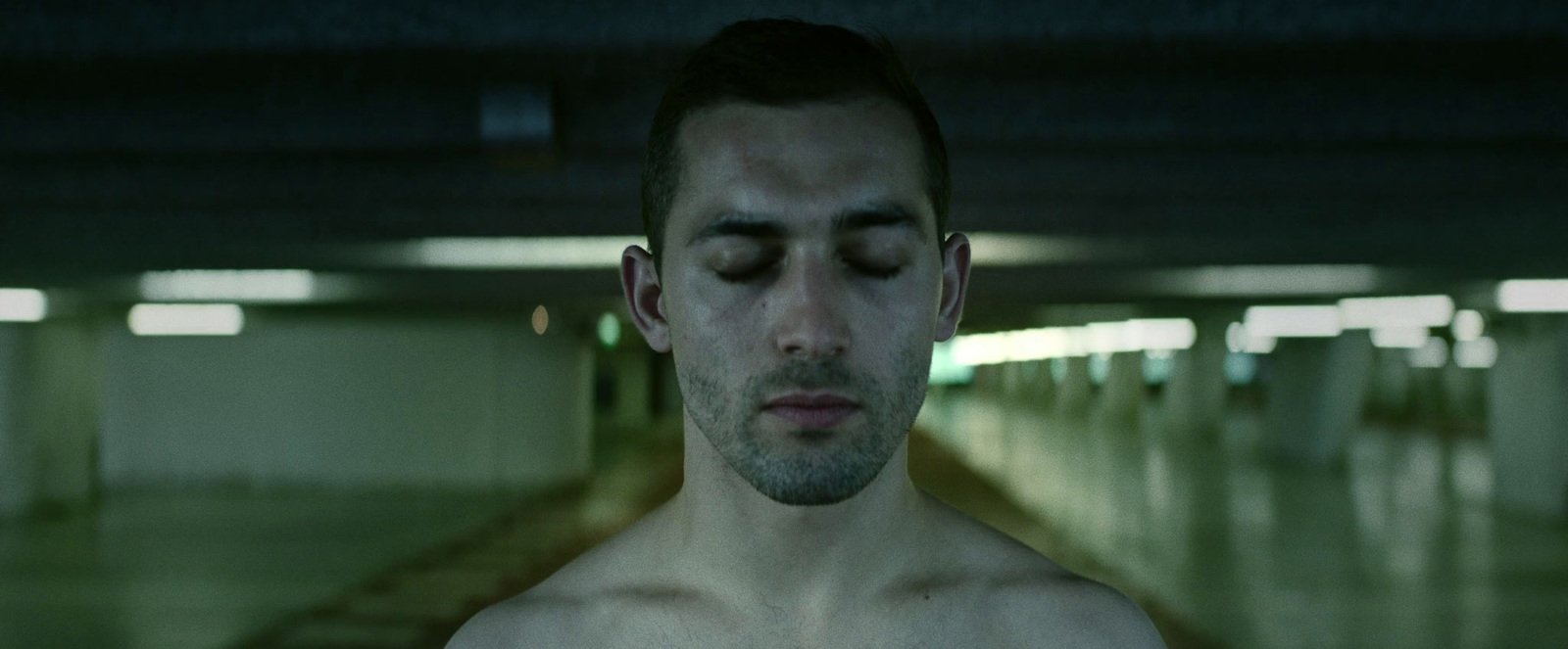 a shirtless man in a parking garage with his eyes closed