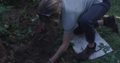 a woman digging in the ground with a garden tool