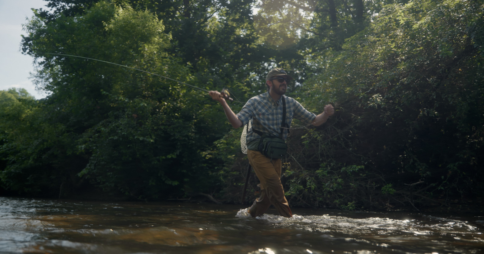 a man standing in a river while holding a fishing rod