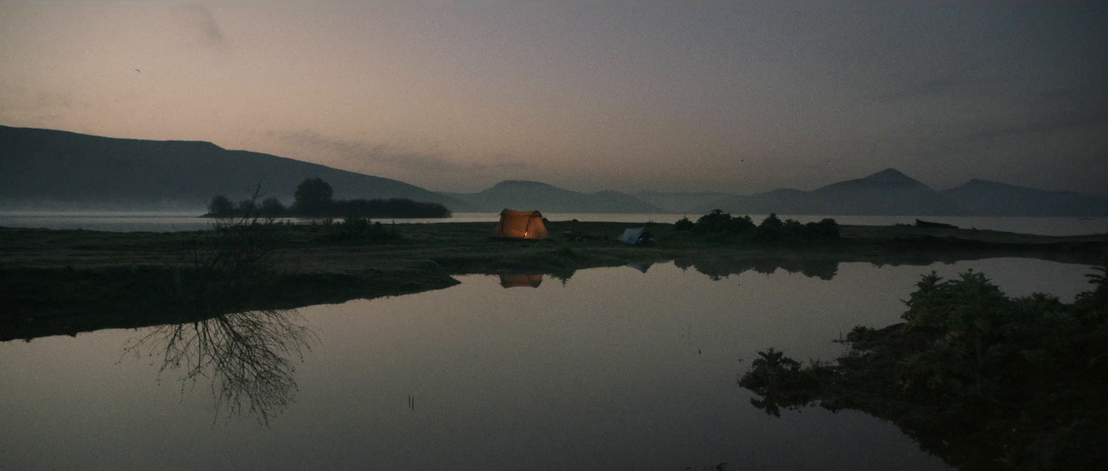 a tent is set up on the shore of a lake