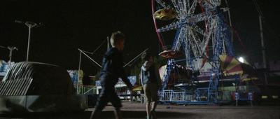 a couple of people walking around a carnival at night