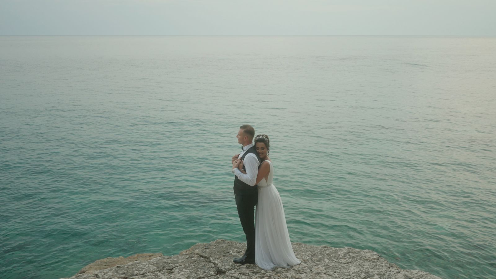 a bride and groom standing on a cliff overlooking the ocean