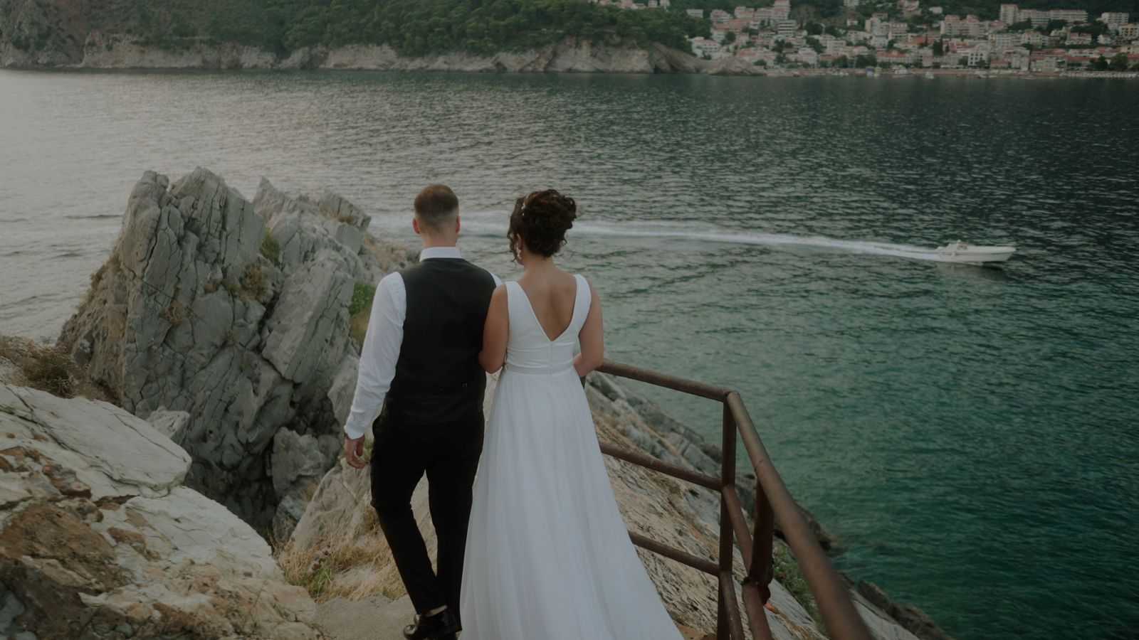 a bride and groom are standing on a cliff overlooking the water