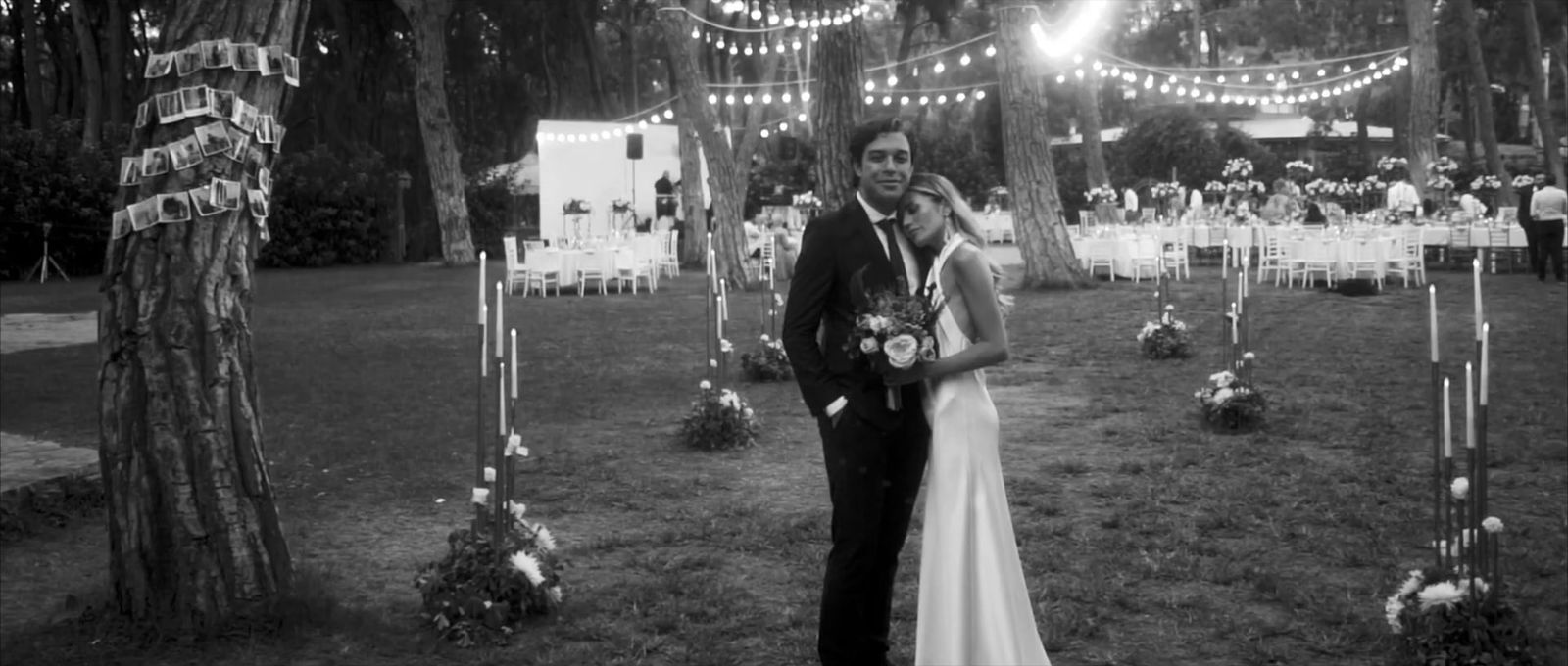 a bride and groom pose for a photo in front of a string of lights