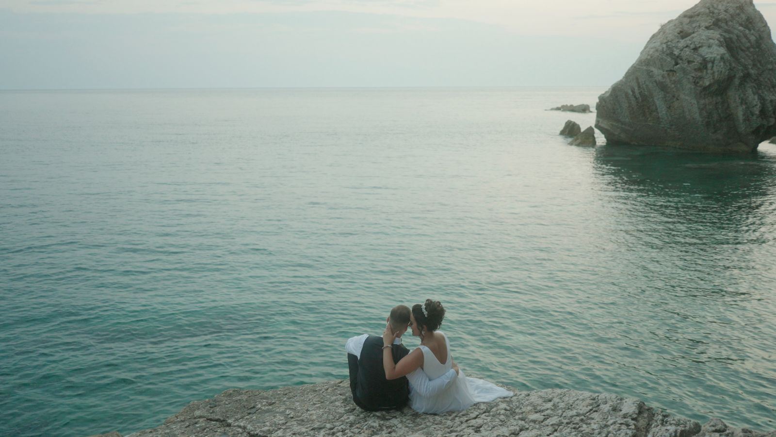 a couple of people sitting on top of a rock near the ocean