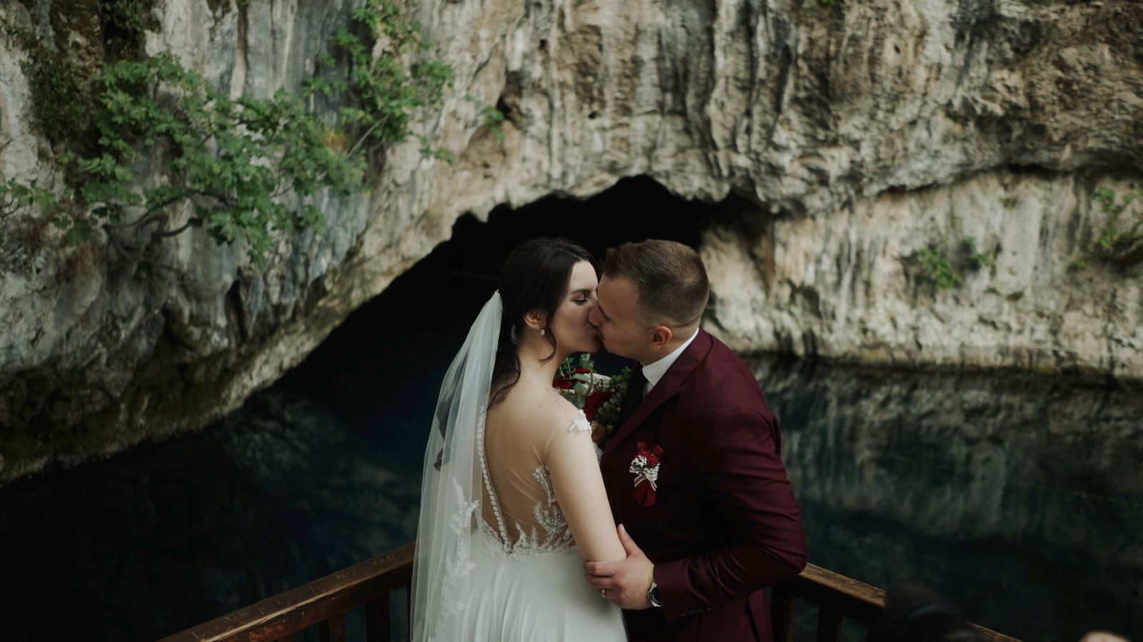 a bride and groom kissing in front of a cave