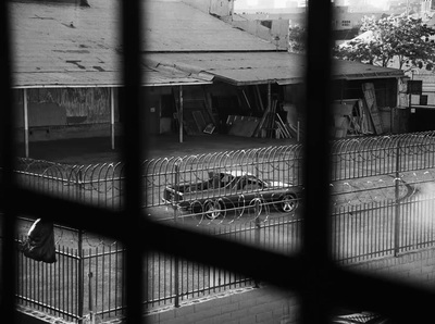 a black and white photo of a car behind a fence