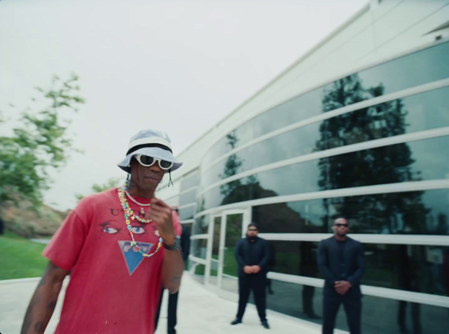 a man wearing a hat and sunglasses standing in front of a building