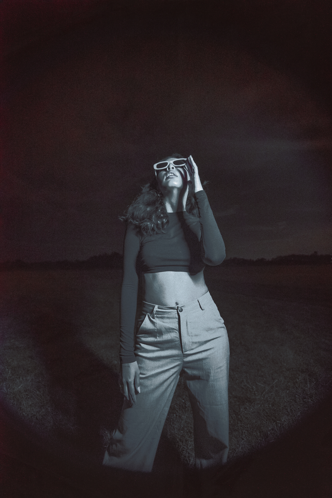 a woman standing in a field holding a camera up to her face