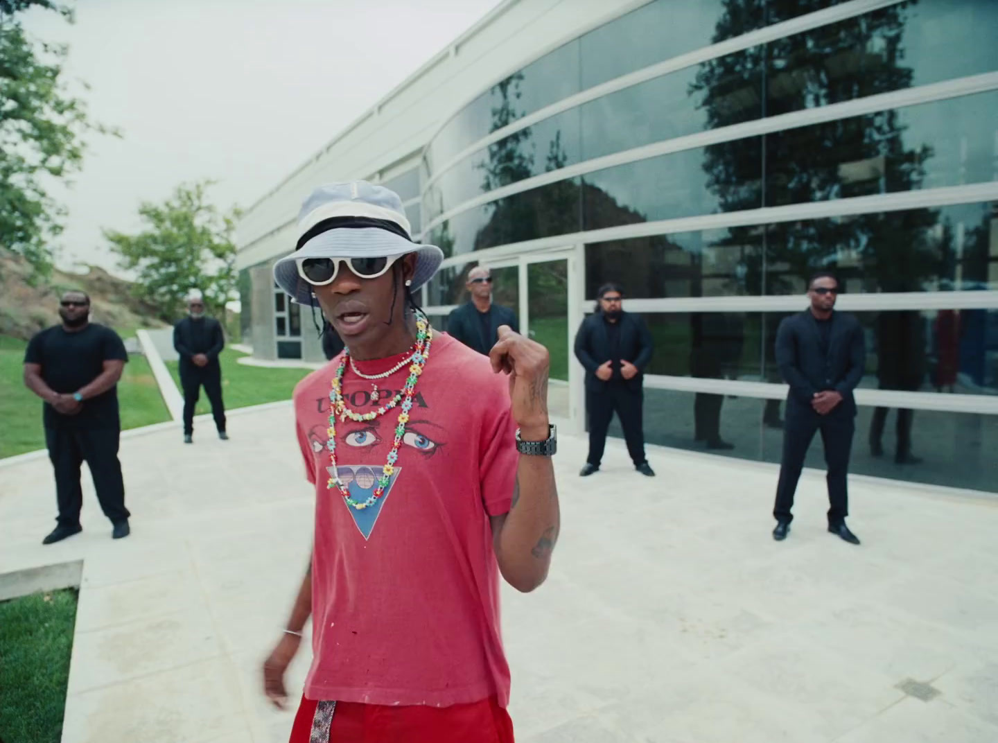 a man wearing a hat and sunglasses standing in front of a building