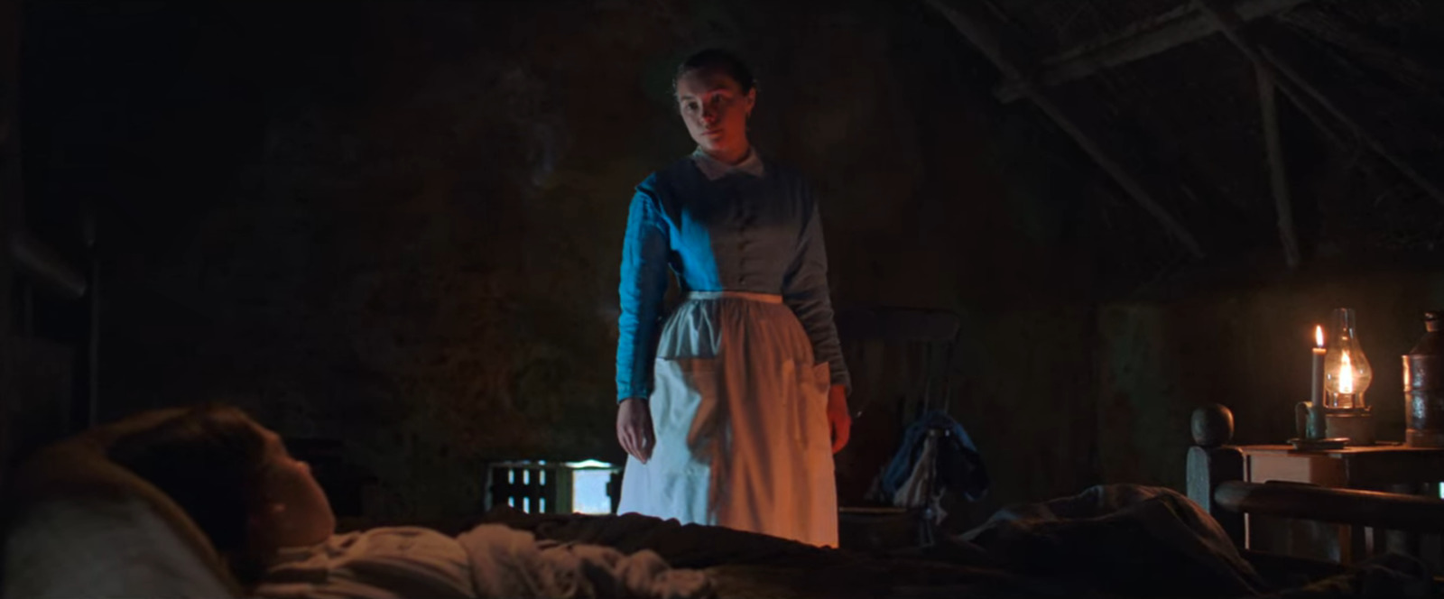 a woman standing in a dark room next to a bed