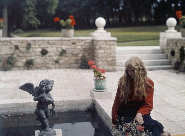 a girl sitting on a ledge looking at a statue