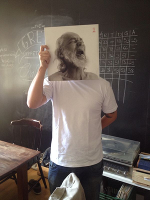 a man holding up a picture of himself in front of a chalkboard