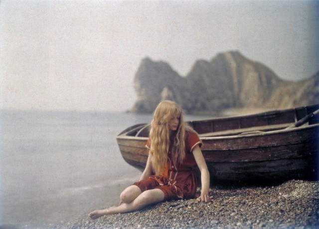 a woman sitting on a beach next to a boat