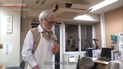 an old man standing in an office talking to someone