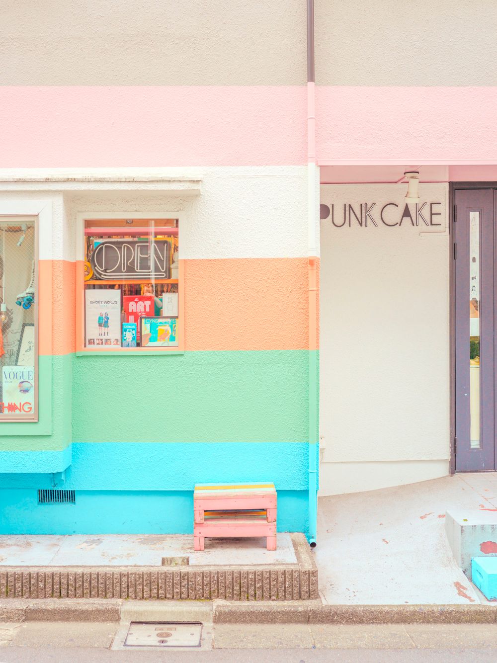 a pink, blue, and green building with a bench in front of it