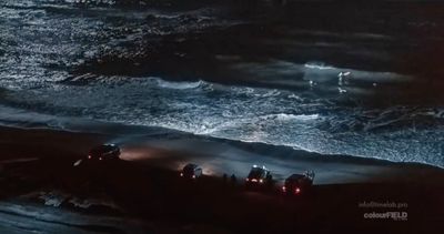 a group of people standing on top of a beach next to the ocean