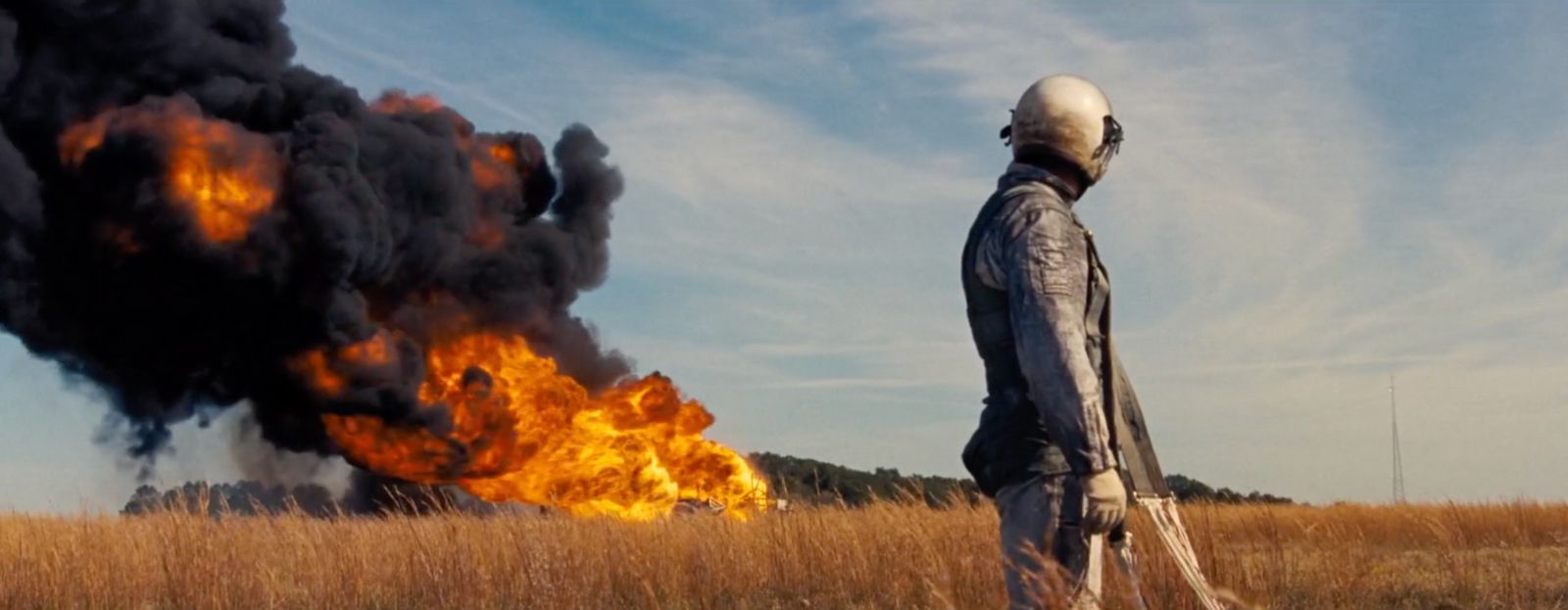 a person standing in a field with a fire in the background