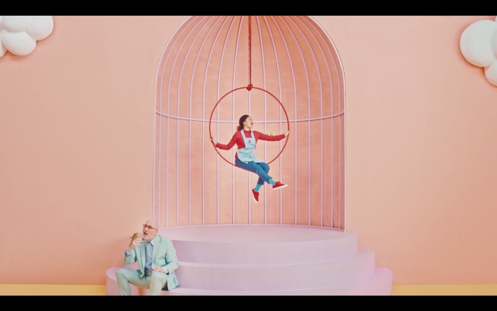 a man and a woman sitting on a chair in front of a birdcage