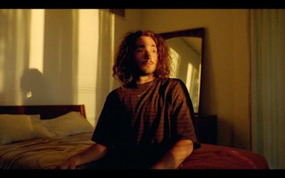 a man with long hair sitting on a bed