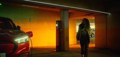 a woman standing in a parking garage next to a red car