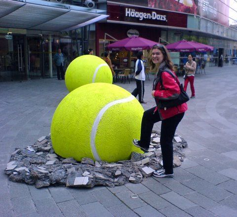 a woman standing next to a giant tennis ball sculpture