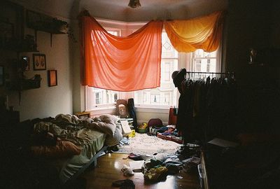 a messy room with a bed and a window