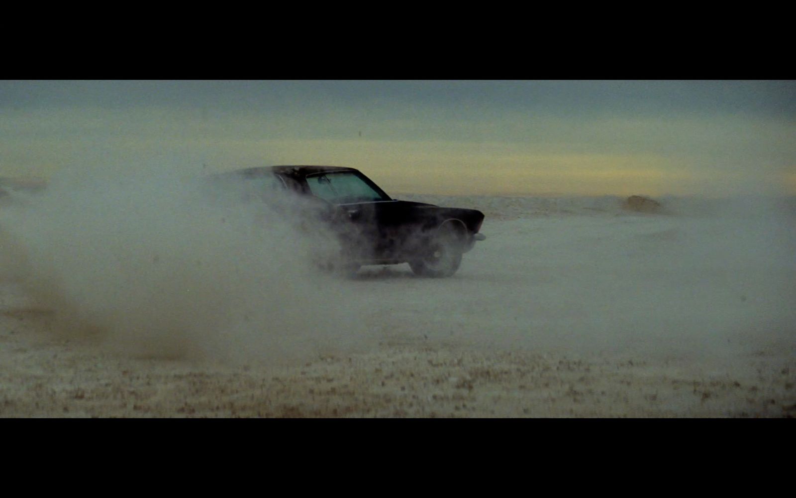 a black car driving through a desert filled with dust