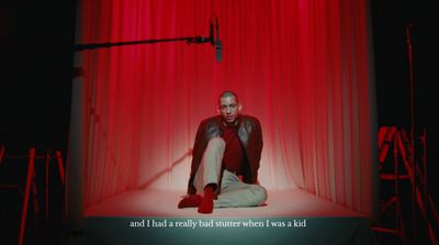 a man sitting on a stage in front of a red curtain