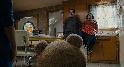 a man and a woman standing in a kitchen with a teddy bear